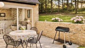 An outdoor patio with a round table, chairs, a grill, and a stone wall. - Cozy cottage in the grounds of an old mill (Payrignac)