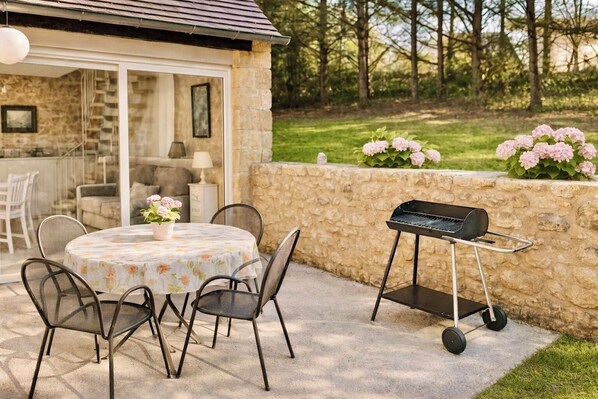 An outdoor patio with a round table, chairs, a grill, and a stone wall.
