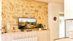A kitchen with a stone wall, a television, a teddy bear, a plant, and a compost bin. - Cozy cottage in the grounds of an old mill (Payrignac)