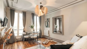 Un salon moderne avec un plancher en bois, un canapé, une table à manger avec des chaises, un téléviseur et un grand miroir au mur.