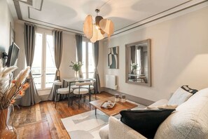 Ein modernes Wohnzimmer mit Holzboden, einer Couch, einem Esstisch mit Stühlen, einem Fernseher und einem großen Spiegel an der Wand.
