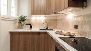 Une cuisine avec des meubles de rangement en bois, un évier noir, un four encastré et un plan de travail sur lequel se trouvent une machine à café et un plateau.