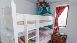 A bunk bed with a lower bunk, a bedside table with a lamp, and a window with curtains. - Pencestyll (Cardigan)