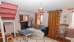 A cozy living room with a sofa, ottoman, and chair, a fireplace, a staircase, and a window with curtains. - Pencestyll (Cardigan)