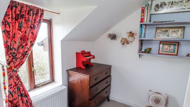 A room with a window, a radiator, a wooden dresser, a small chair, and a shelf with framed pictures. - Pencestyll (Cardigan)