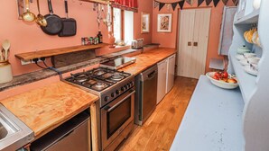 A kitchen with a gas stove, oven, and dishwasher, wooden countertops, and a hanging pot rack. - Pencestyll (Cardigan)