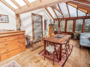 A room with a wooden dining table, chairs, a wooden dresser, and a large window with a view of trees. - Pencestyll (Cardigan)