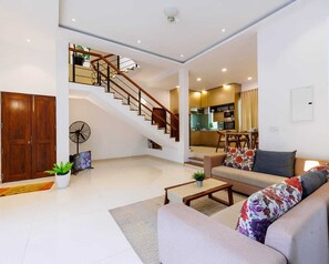 A spacious living area with a staircase, a sofa, a coffee table, and a fan.