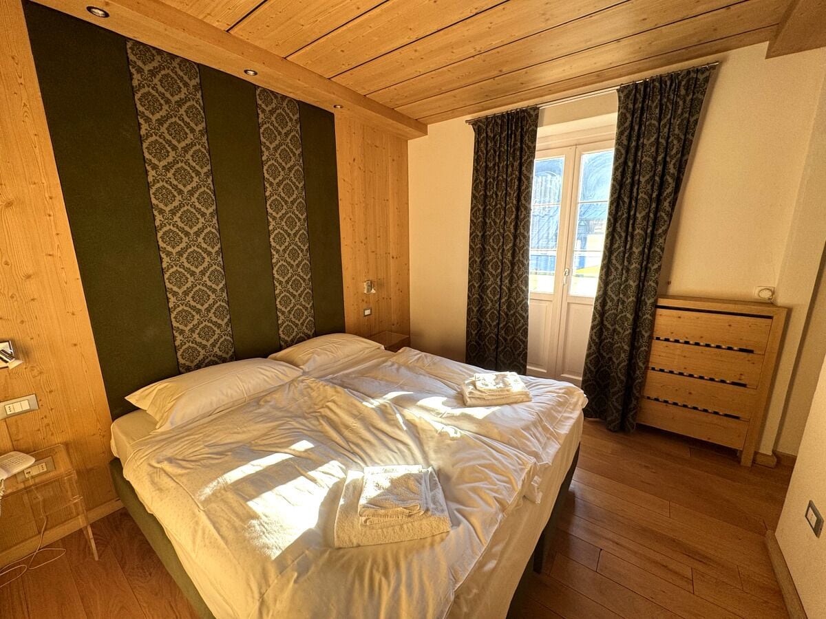 Una habitació amb sostre de fusta, llit amb roba blanca, taulell de vestir de fusta i cortines estampades.