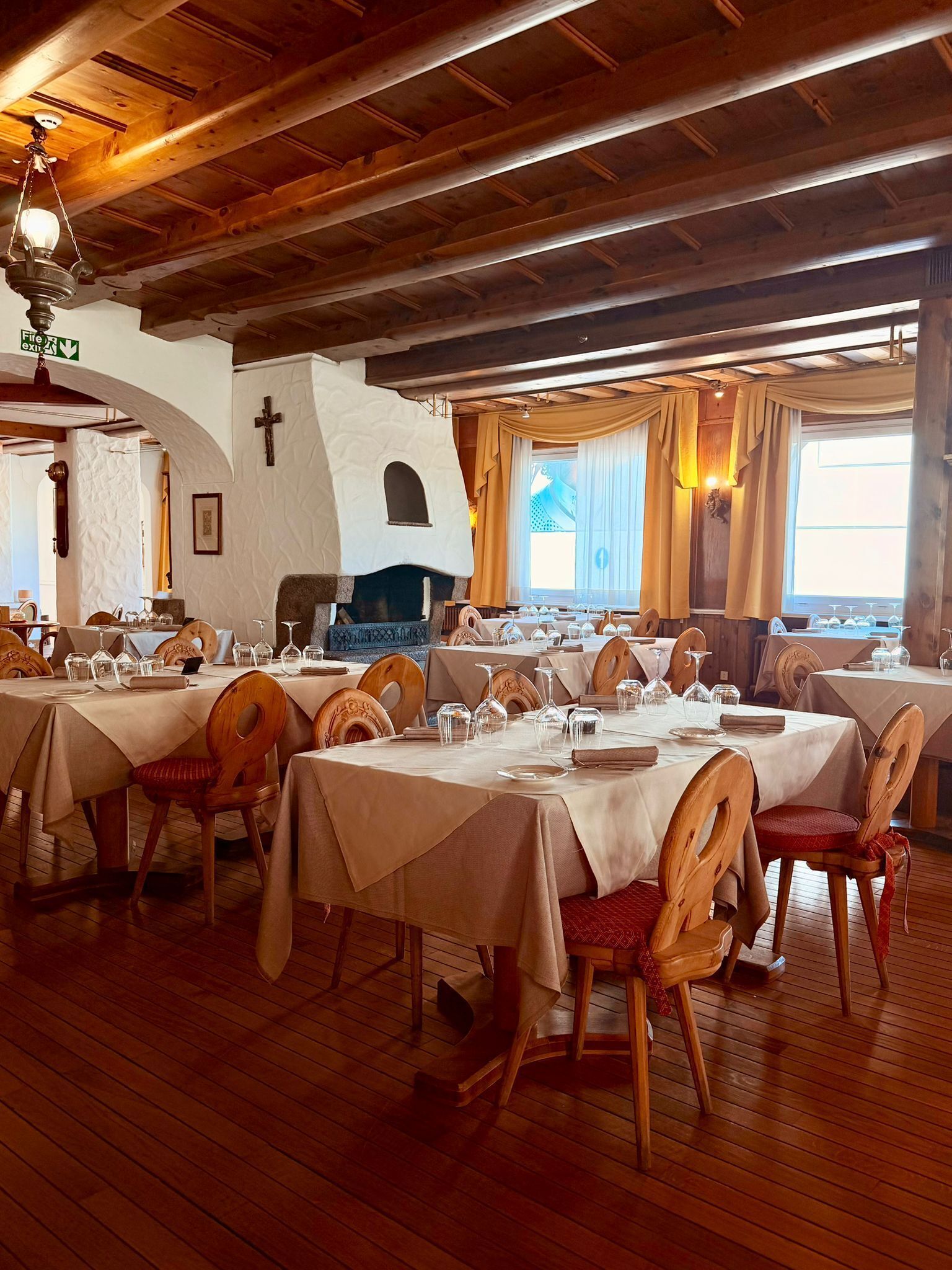 A restaurant with wooden tables and chairs, a fireplace, and a cross on the wall.