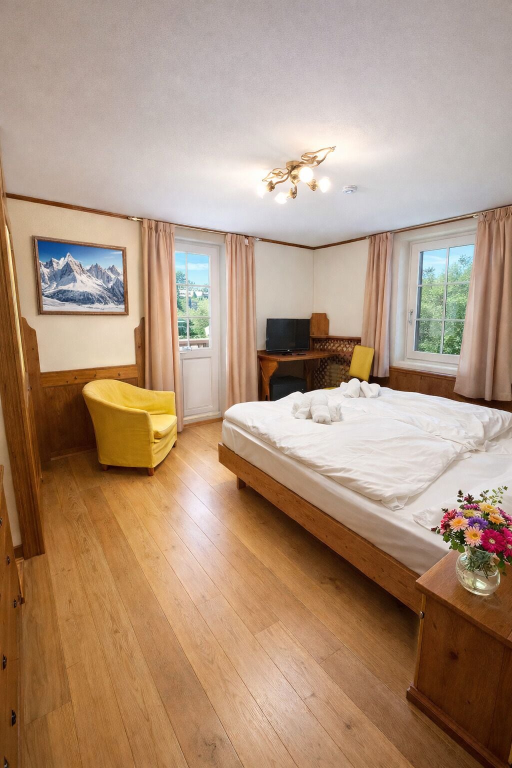 Un dormitorio con cama, una silla, escritorio con televisor, un cuadro y una ventana.