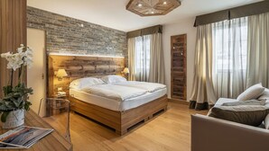 A modern bedroom with a wooden bed, a desk, and a chair, featuring a brick wall and large windows. - Parc Hotel Victoria (Cortina d'Ampezzo)
