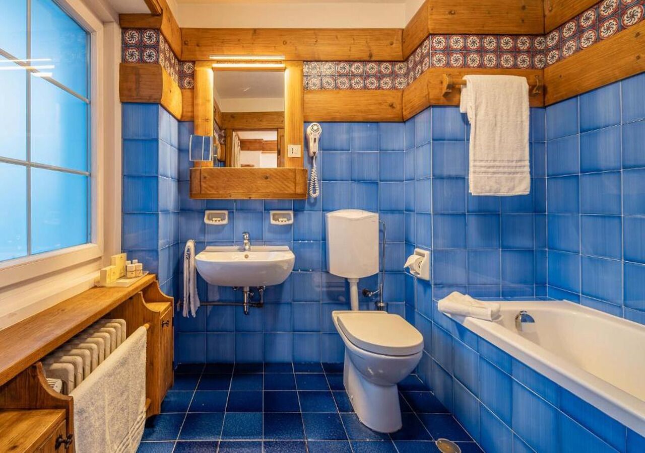 A bathroom with blue tiles, a wooden vanity, a sink, a toilet, and a bathtub.