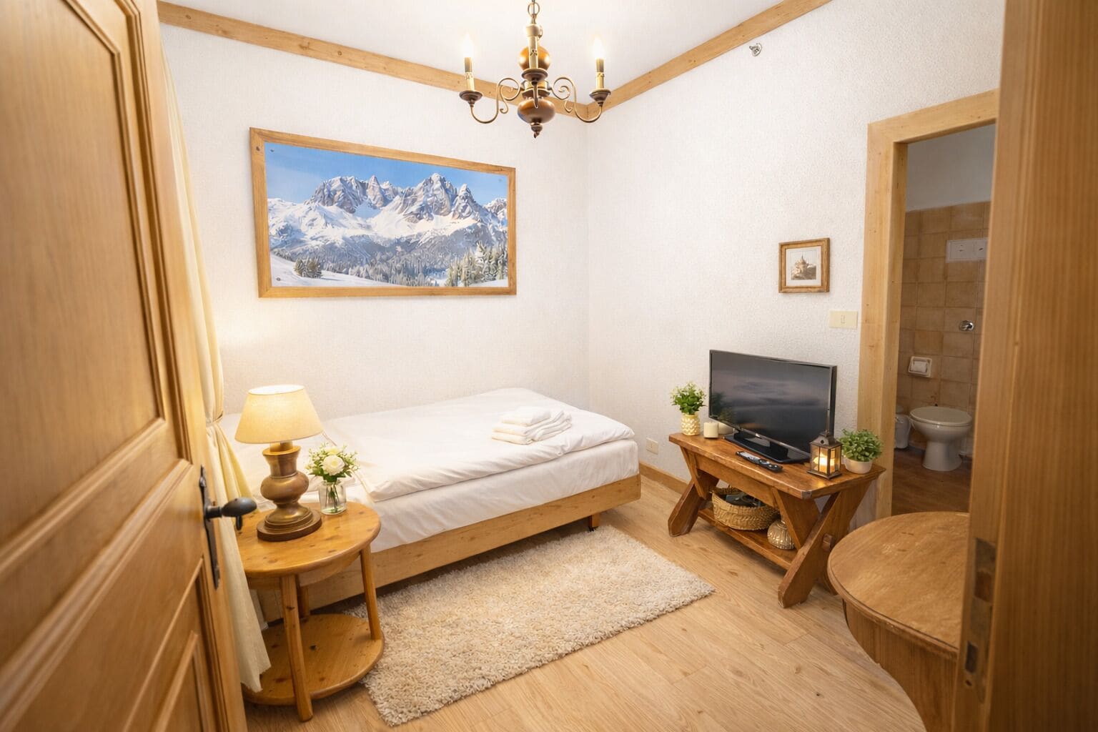 A bedroom with a bed, a TV, a lamp, a painting, and a small table with a plant.