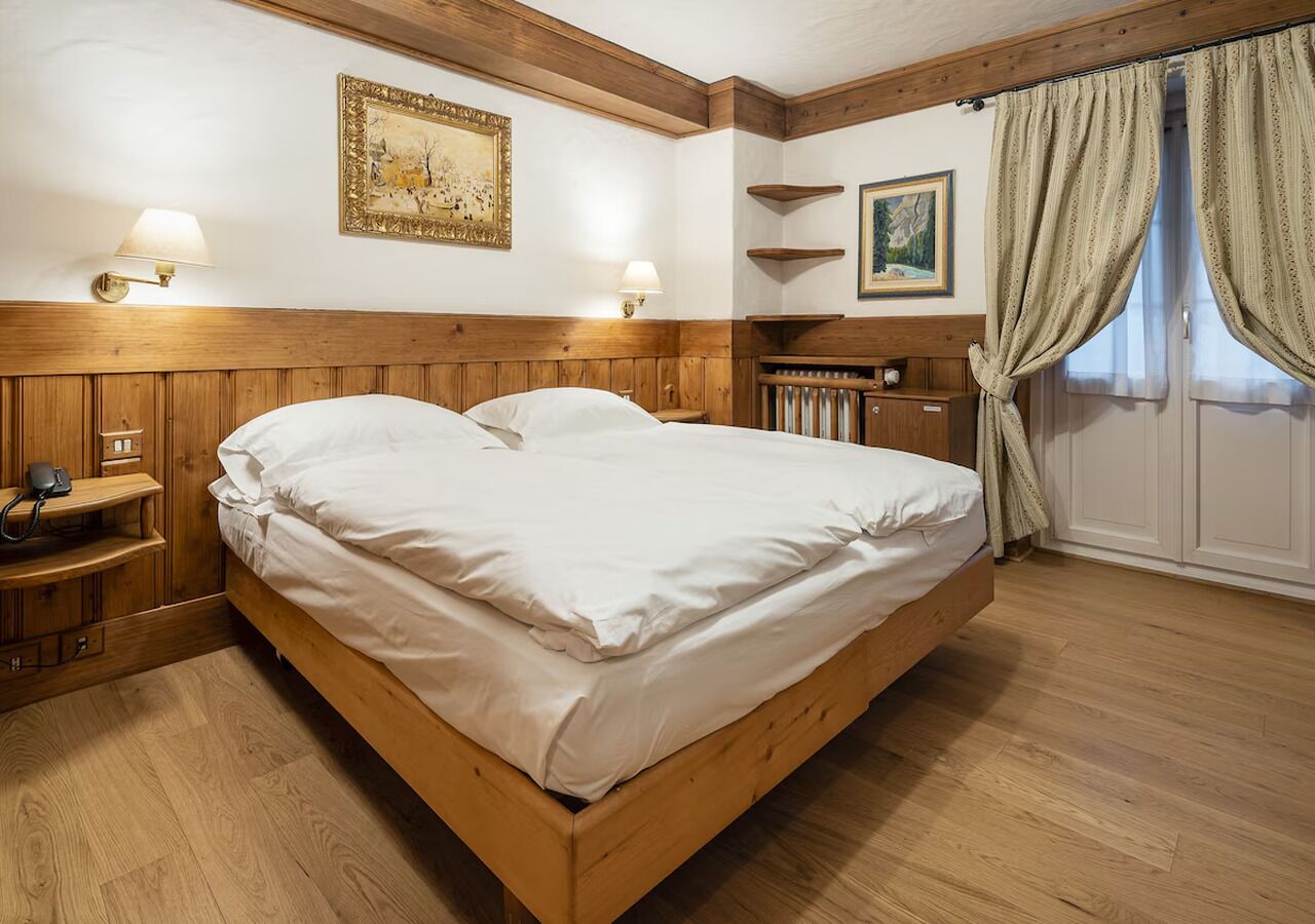 Un lit en bois dans une chambre avec une tête de lit en bois, deux lampes fixées au mur et un tableau au-dessus du lit.