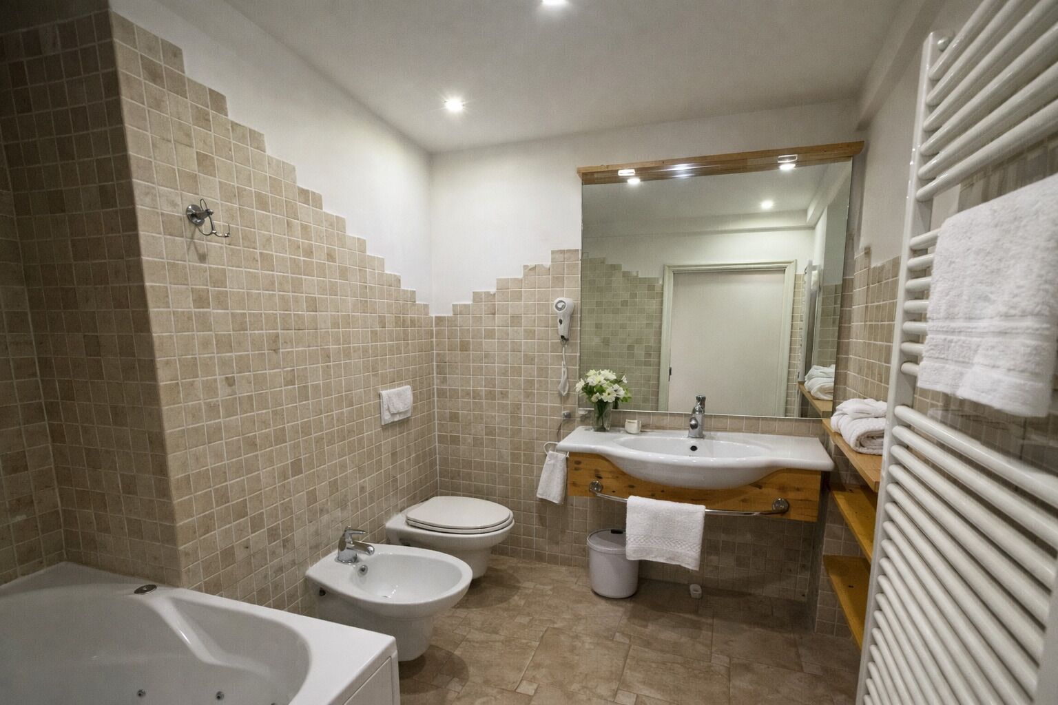 A bathroom with a bathtub, two toilets, a sink, and a mirror.