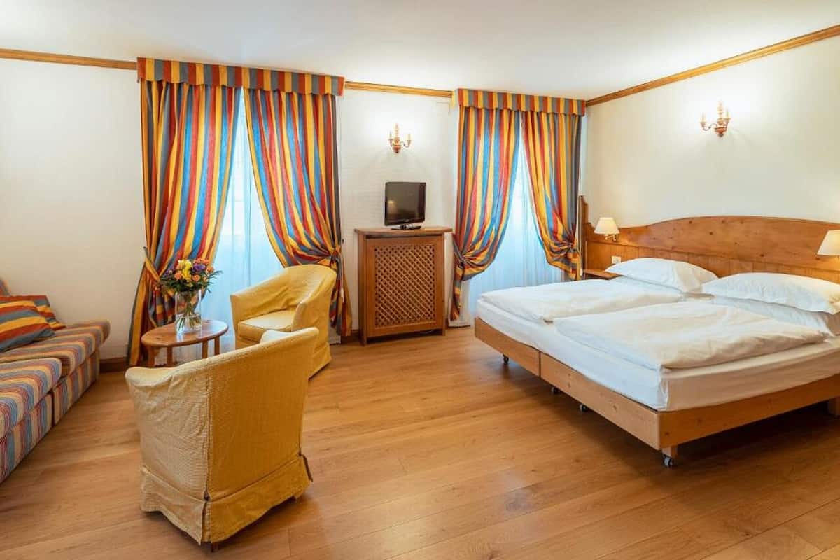A hotel room with a bed, a sofa, a chair, a TV, and curtains.