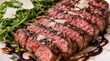 A plate of sliced steak with a dark sauce, garnished with lemon and greens, on a white plate.