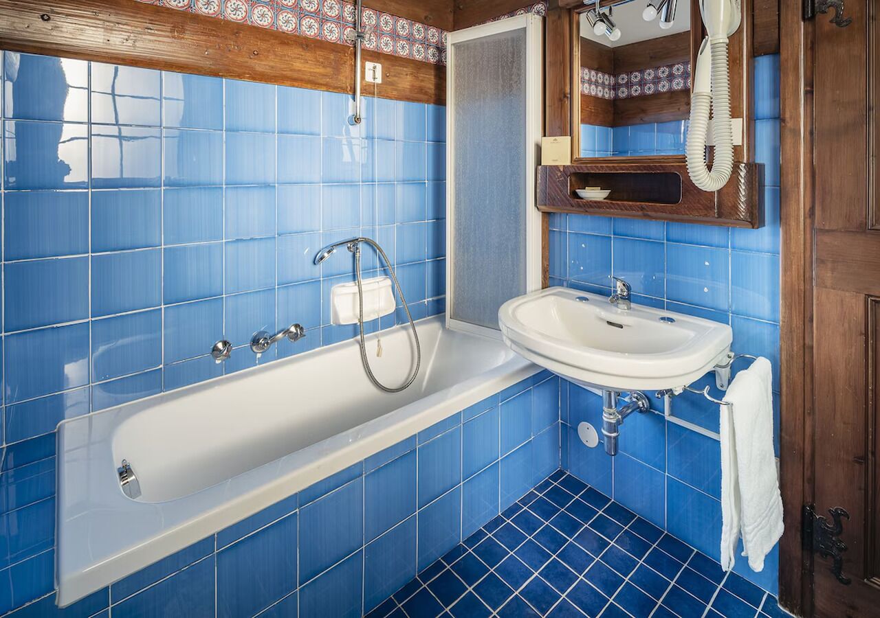A bathroom with blue tiles, a white bathtub, a white sink, and a wooden door.