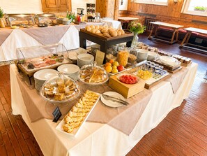 Una mesa de buffet con diversos alimentos, como pasteles, frutas y salsas, dispuesta en un espacio con suelo y muebles de madera.