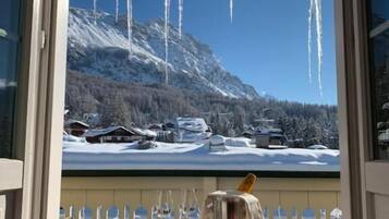 A table with a bottle and glasses, a view of a snowy mountain landscape through a window, and icicles hanging from the window frame.