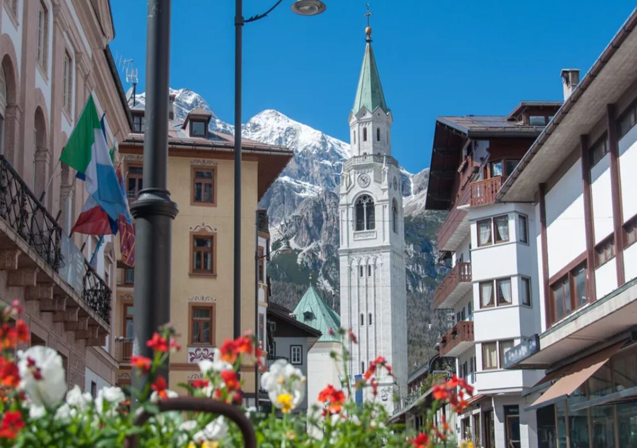 Un pueblo de montaña con una iglesia, edificios y montañas nevadas al fondo.