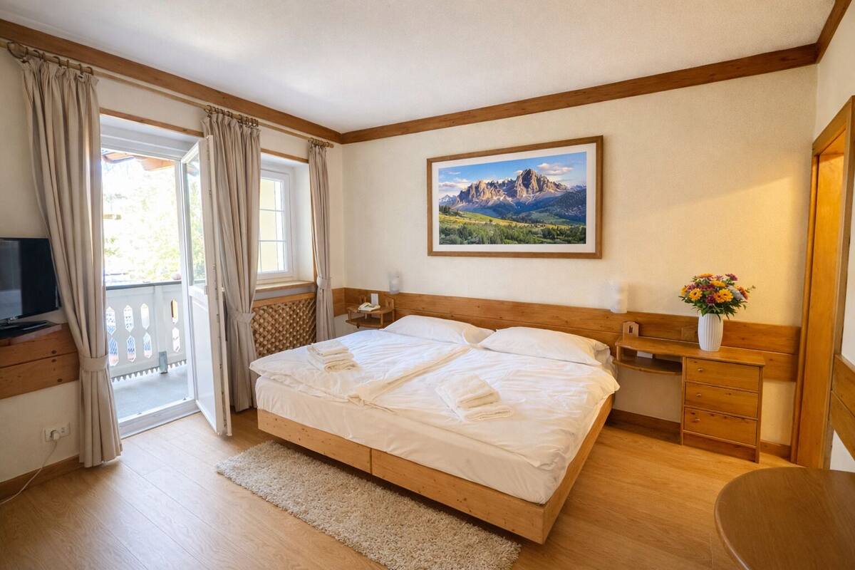 A bedroom with a bed, a desk, a chair, a TV, a window with curtains, and a painting on the wall.