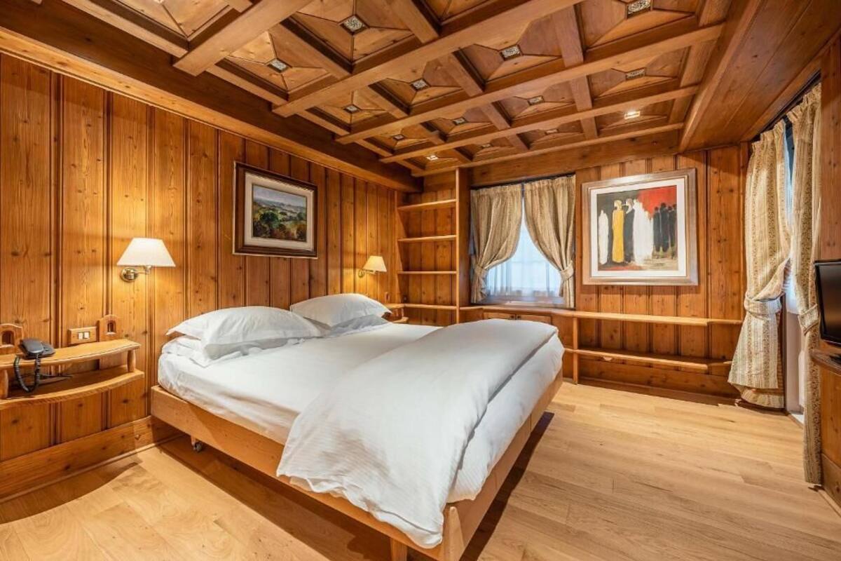 A wooden-paneled room with a bed, bedside lamps, a shelf, and a painting.