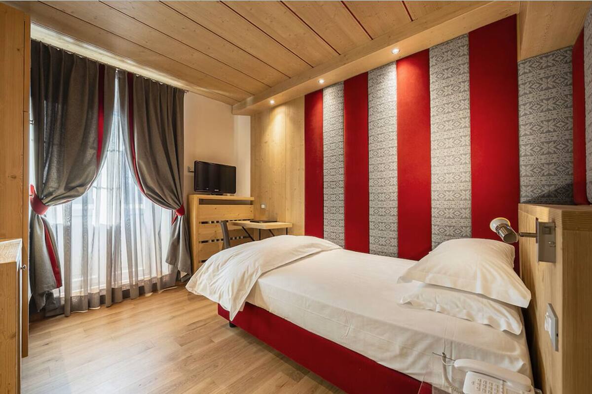 A room with a bed, a desk, a television, and a window with curtains.