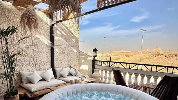 Huone, jossa on poreallas, tyynyillä varustettu sohva, ruukkukasvi ja näkymä pyramideille.