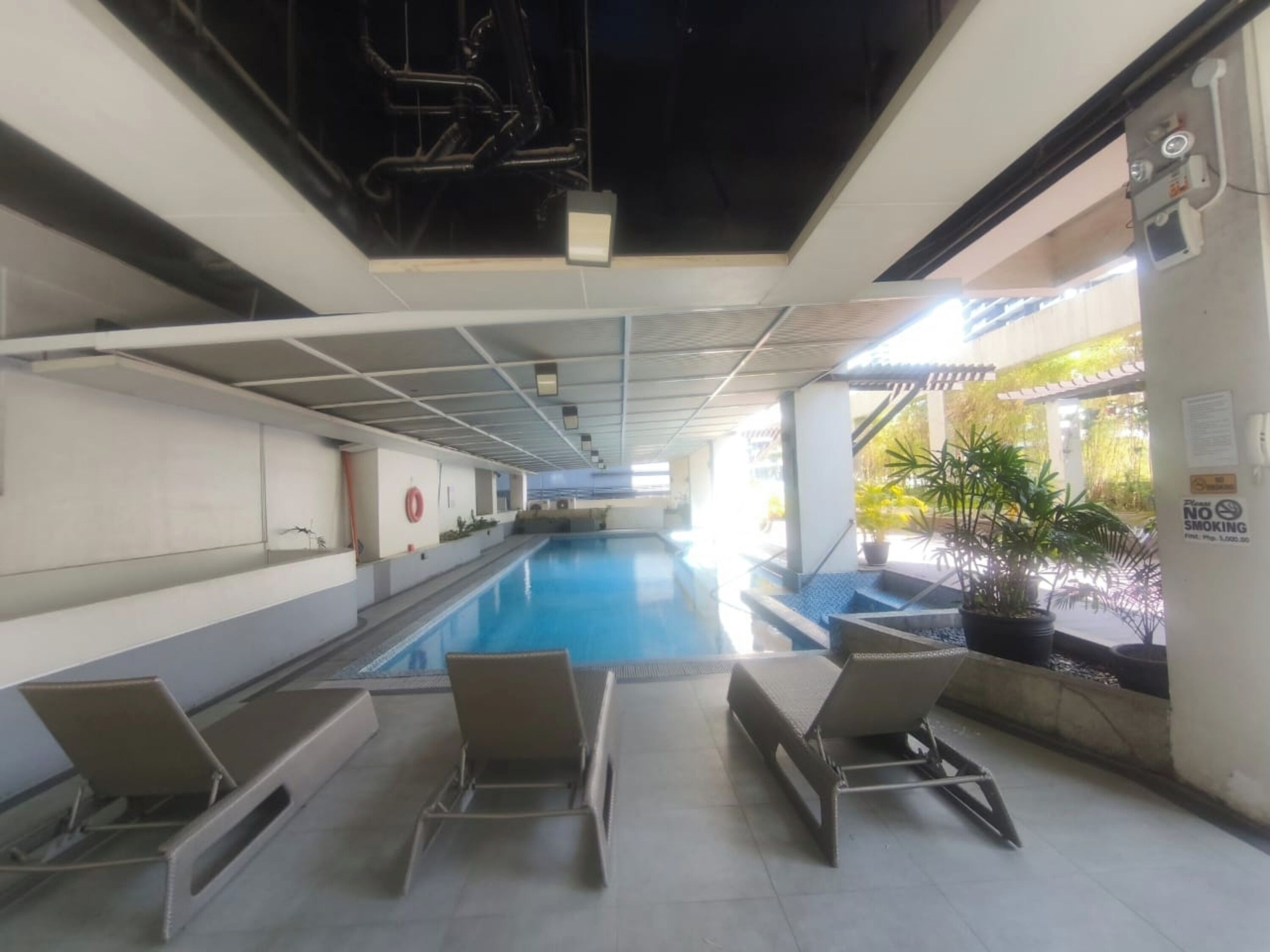 An indoor swimming pool with lounge chairs, a lifebuoy, and a 'No Smoking' sign.