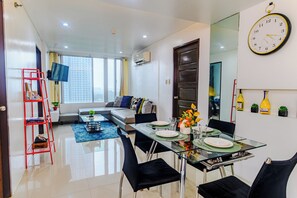 A modern living room with a sofa, a dining table set for two, and a large wall clock. - Cozy City Stays at Seibu Tower (Taguig)