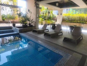 An indoor pool area with a clear view of the pool, lounge chairs, and surrounding greenery. - Cozy City Stays at Seibu Tower (Taguig)