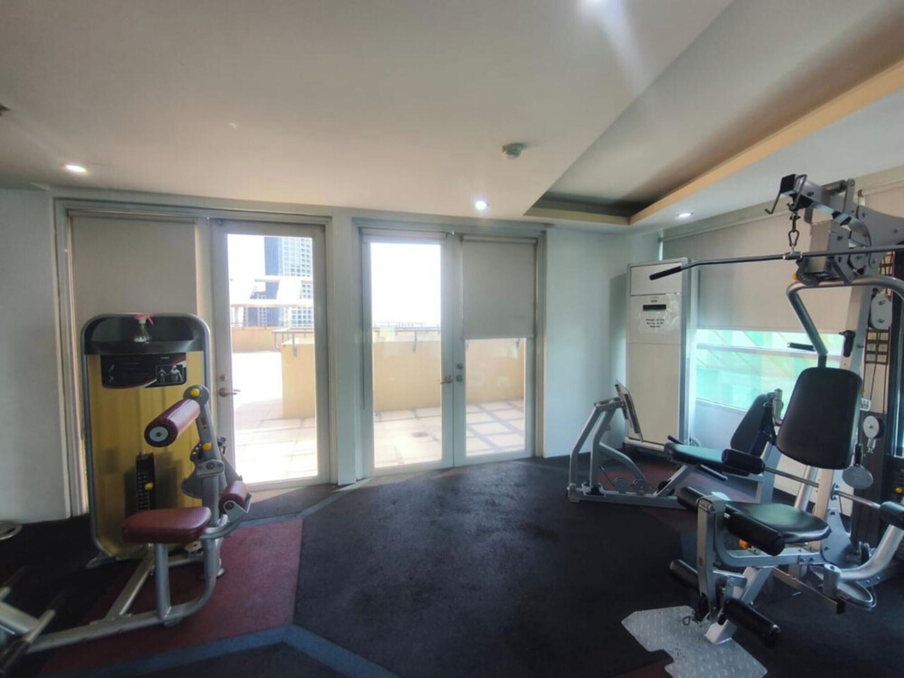 A gym with exercise equipment, a sliding glass door leading to an outdoor area, and a view of buildings outside.