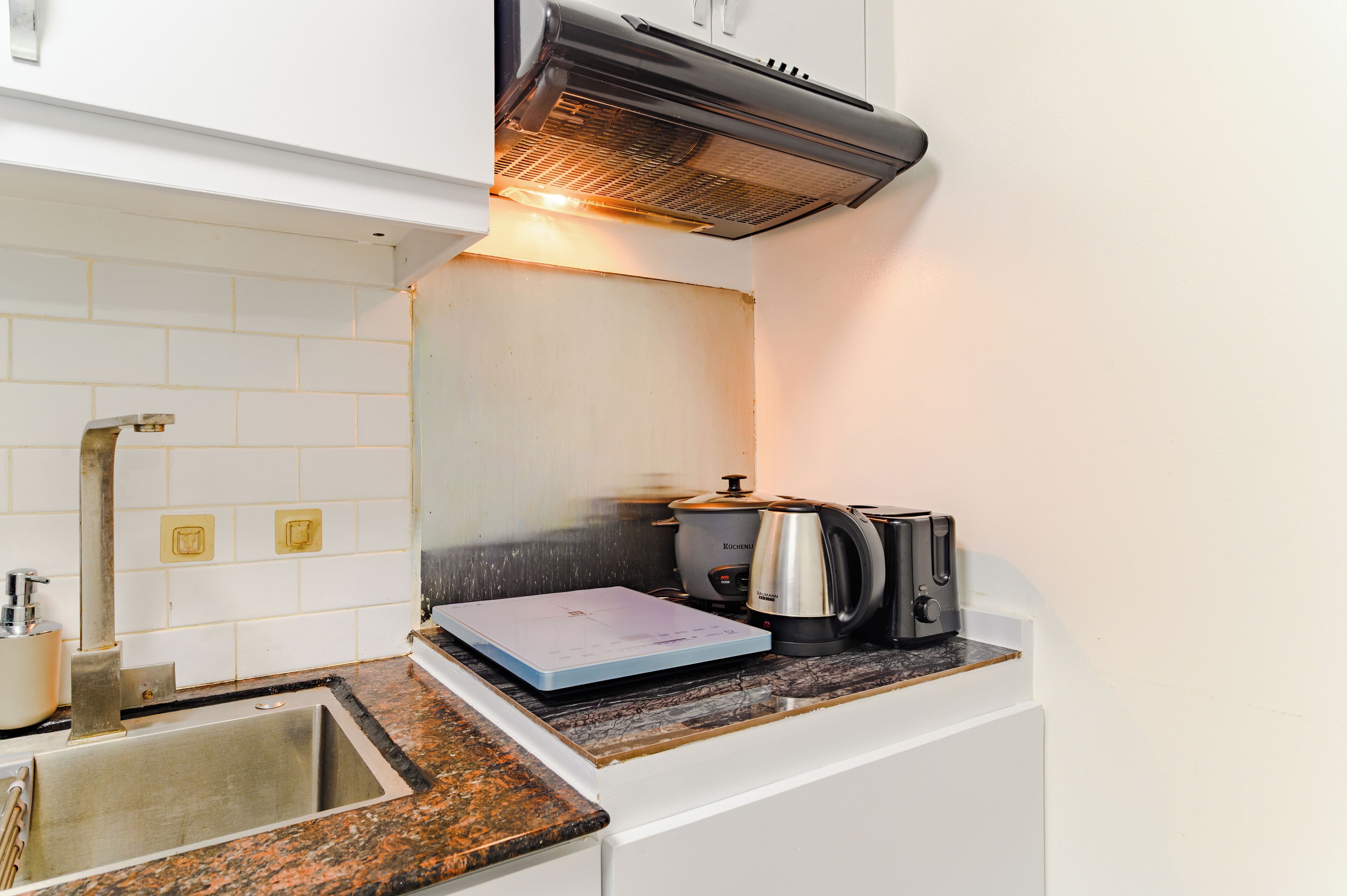 A kitchen with a built-in oven, a kettle, a toaster, and a scale on the countertop.