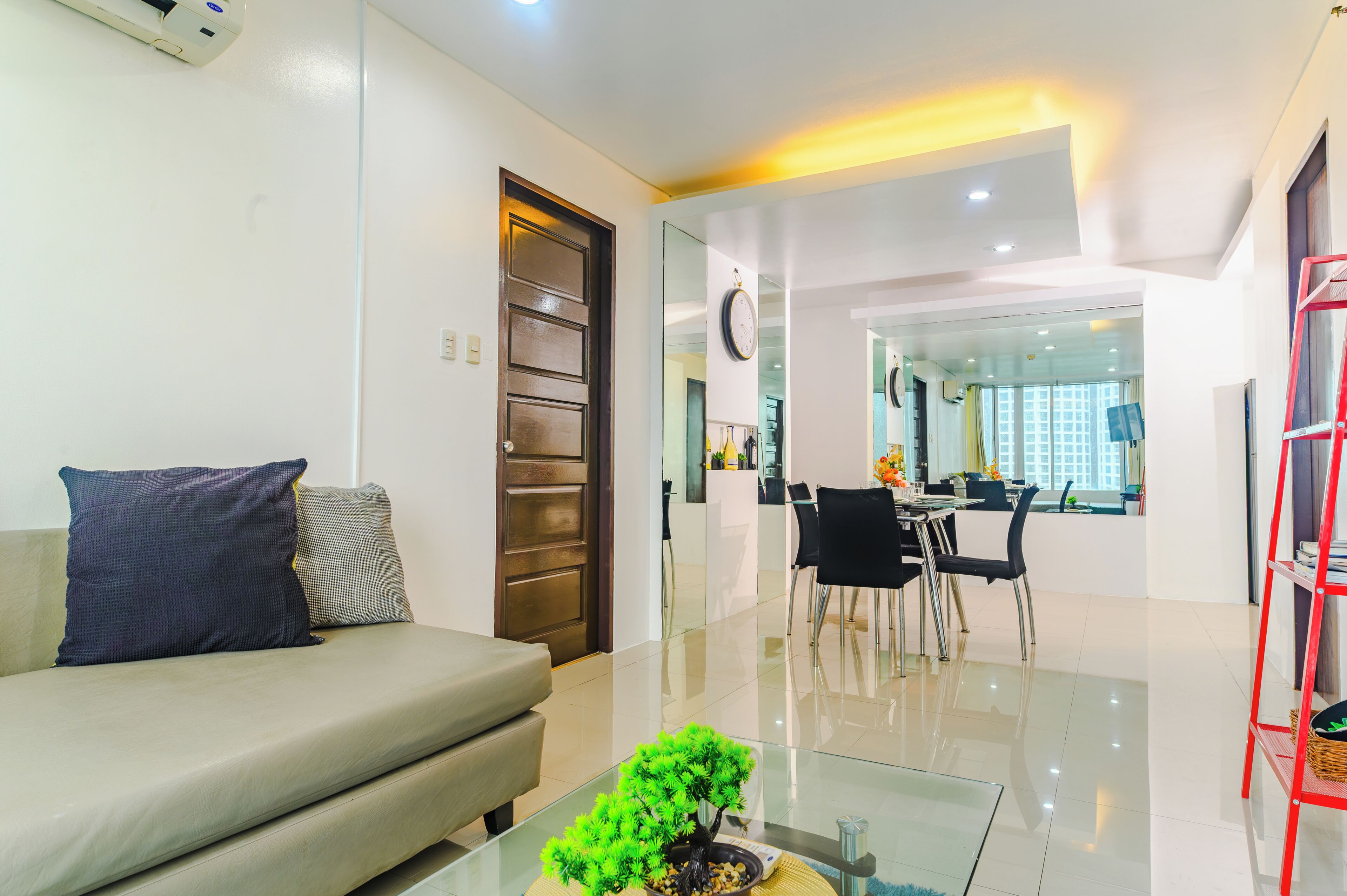 A modern living room with a sofa, a glass coffee table, and a dining area with chairs and a table.