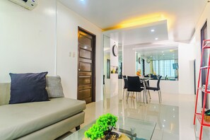 A modern living room with a sofa, a glass coffee table, and a dining area with chairs and a table. - Cozy City Stays at Seibu Tower (Taguig)