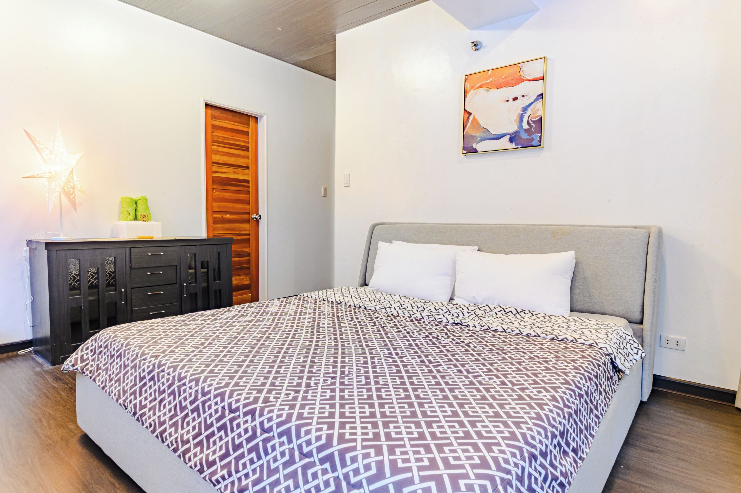 A bedroom with a bed, a nightstand, a lamp, and a painting on the wall.