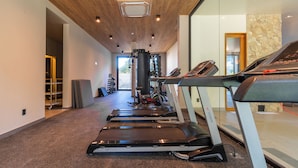 Une salle de sport équipée de tapis de course, de poids et d’un mur en pierre.