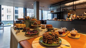 Un buffet proposant une variété de desserts et de boissons, un espace détente avec des tables et des chaises, et une vue sur les bâtiments environnants.