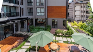 Une cour avec une terrasse en bois, des sièges d’extérieur et une vue sur des immeubles modernes.