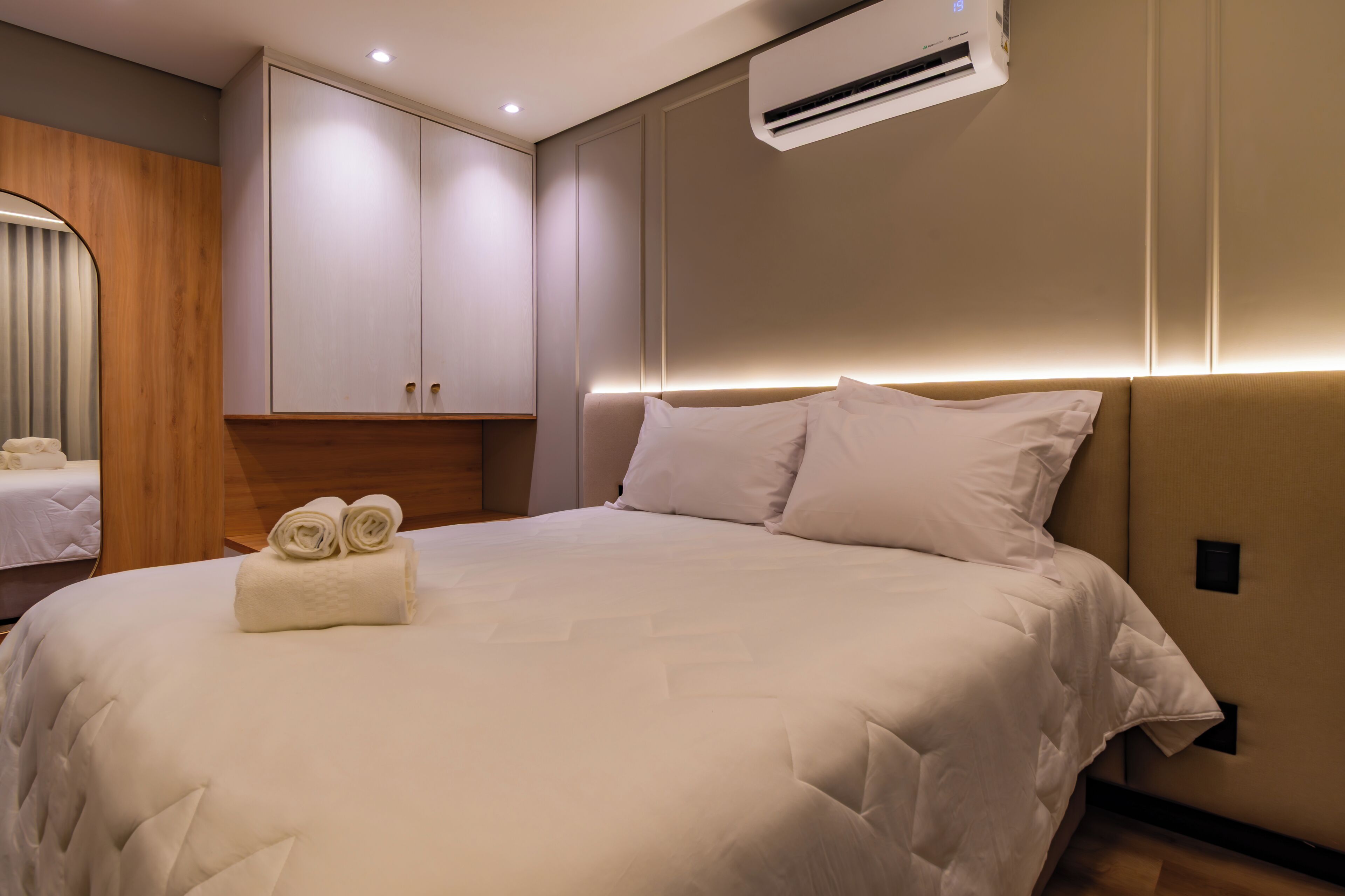 A neatly made bed with a headboard, a wall-mounted air conditioner, and a wooden panel on the left.