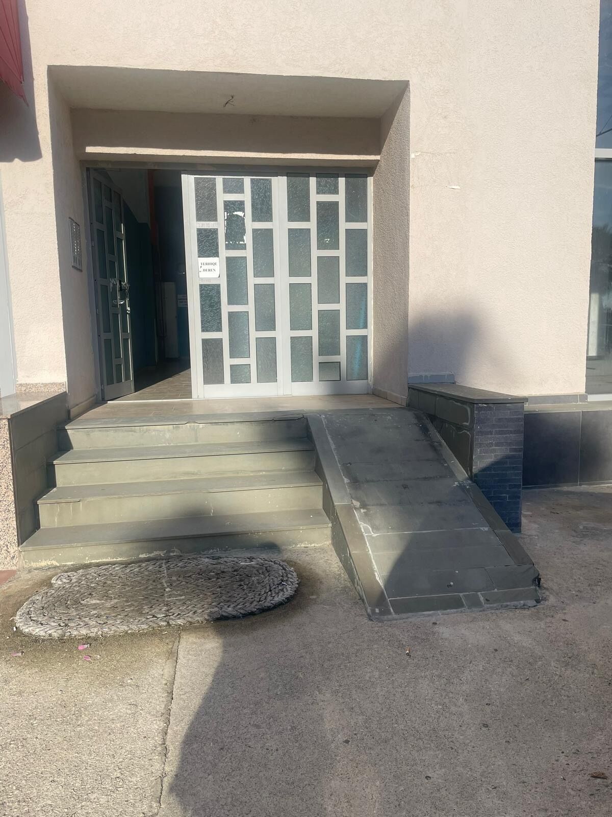 A building entrance with a set of concrete steps leading up to a glass door with a metal gate.