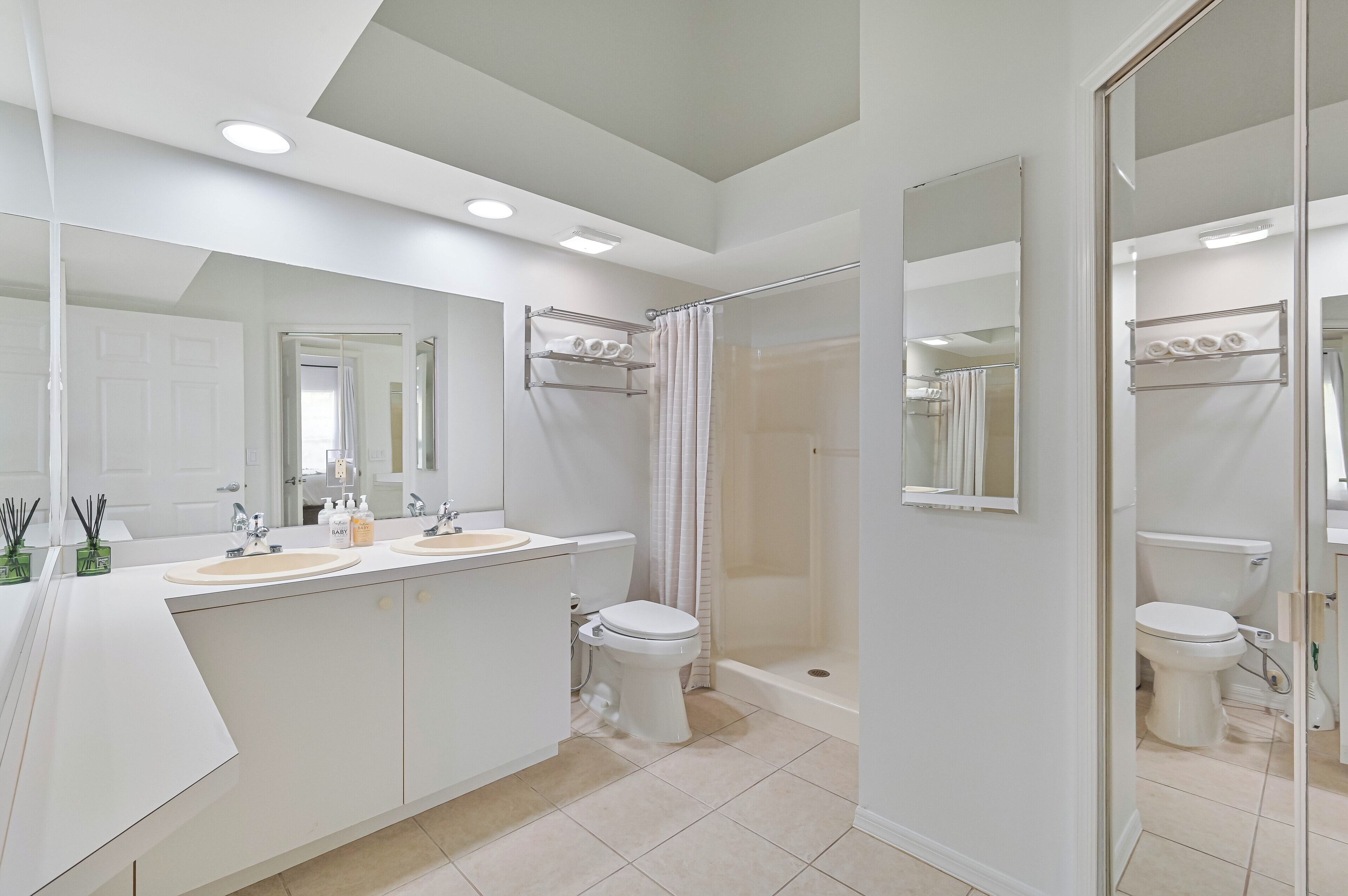 A modern bathroom with a large mirror, two sinks, a toilet, and a shower area.