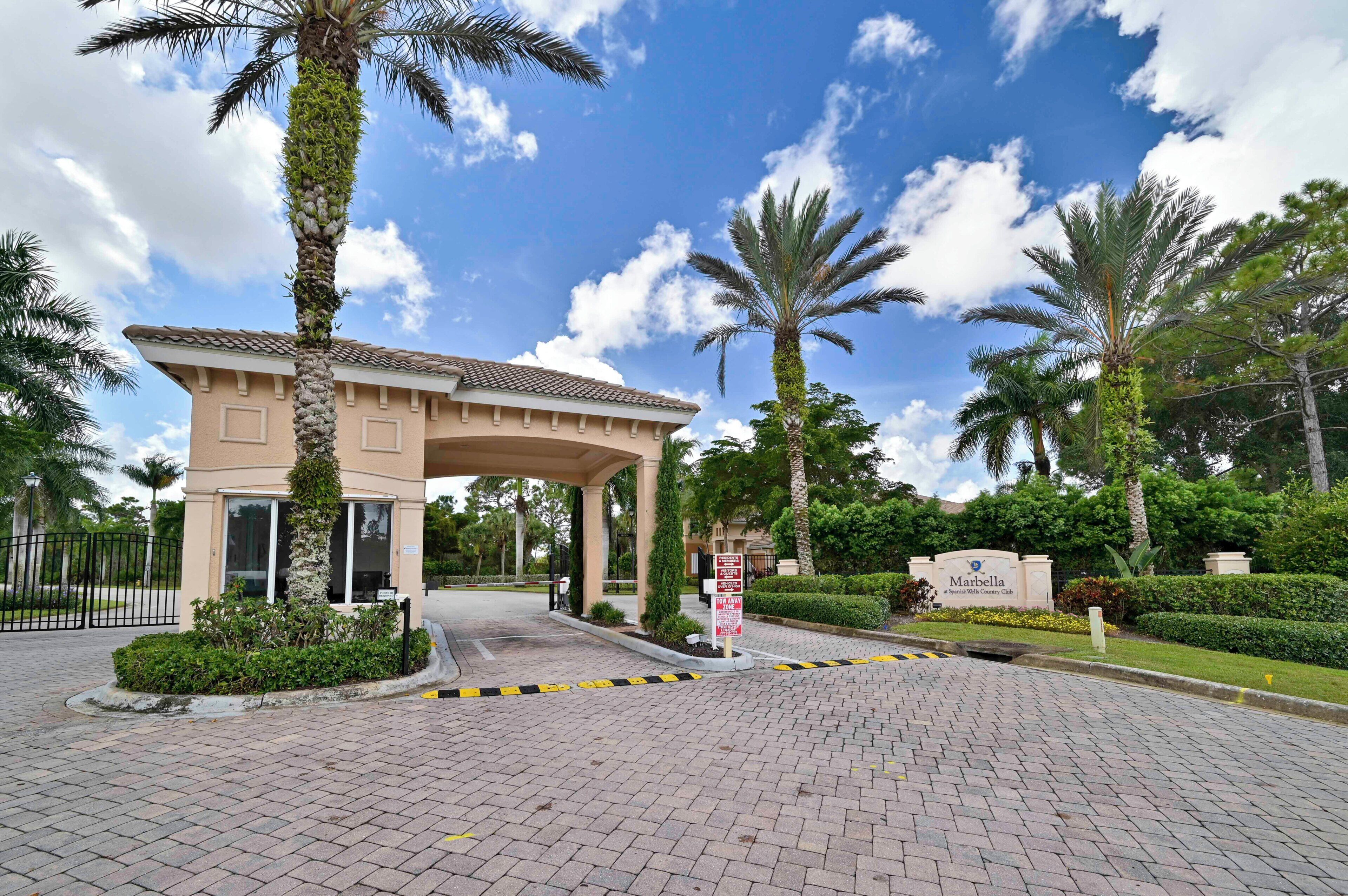A gated entrance to a property with a covered walkway, palm trees, and a sign indicating a 'Tow Away Zone.'