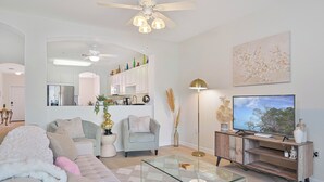 Ein modernes Wohnzimmer mit einem Glastisch, einer Couch, einem Fernseher und einem Deckenventilator.