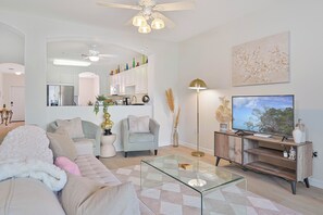 Ein modernes Wohnzimmer mit einem Glastisch, einer Couch, einem Fernseher und einem Deckenventilator.