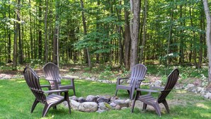 Deux fauteuils Adirondack placés face à face, avec un foyer au centre, le tout entouré d’une pelouse et bordé d’arbres en arrière-plan.