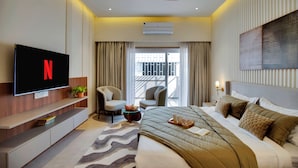 A modern hotel room with a flat-screen TV, a bed with a quilted cover, a ceiling fan, and a view of the outside. - ELIVAAS 3 BHK Villa Shourya Bliss (Udaipur)