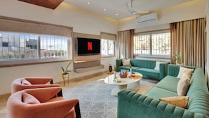 A modern living room with a flat-screen TV, green sofas, a coffee table, and a patterned rug. - ELIVAAS 3 BHK Villa Shourya Bliss (Udaipur)